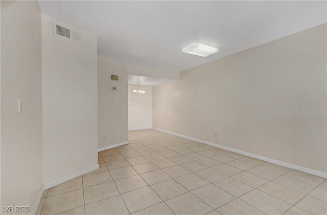 tiled spare room with a notable chandelier