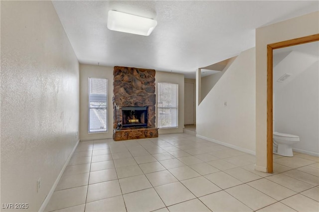 unfurnished living room featuring a stone fireplace, light tile patterned flooring, and a healthy amount of sunlight