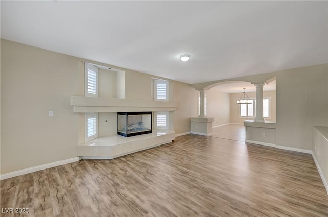 unfurnished living room featuring a multi sided fireplace, ornate columns, and hardwood / wood-style floors