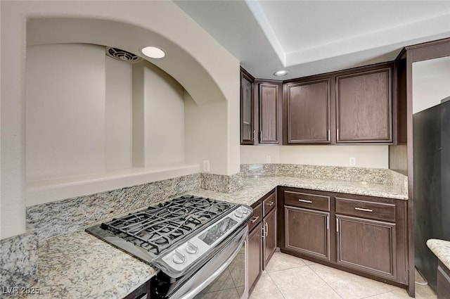 kitchen featuring dark brown cabinets, stainless steel stove, light tile patterned floors, and light stone counters