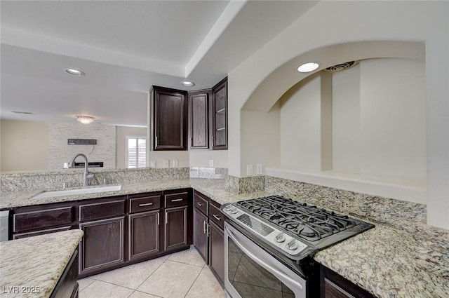 kitchen featuring sink, light tile patterned floors, a fireplace, stainless steel range, and dark brown cabinetry