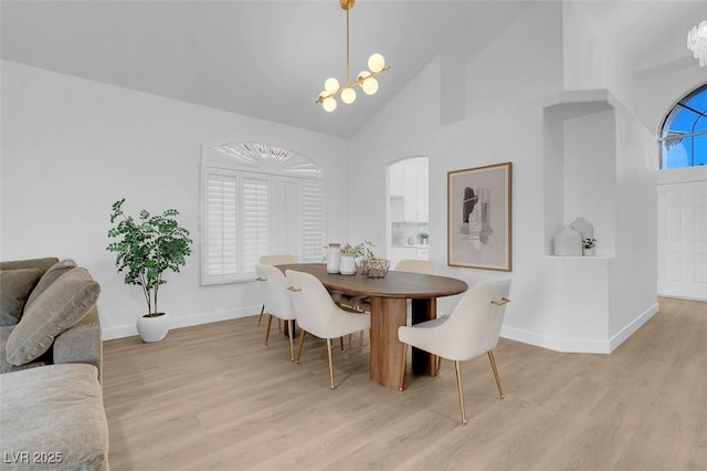 dining room with a notable chandelier, light wood-type flooring, and a towering ceiling