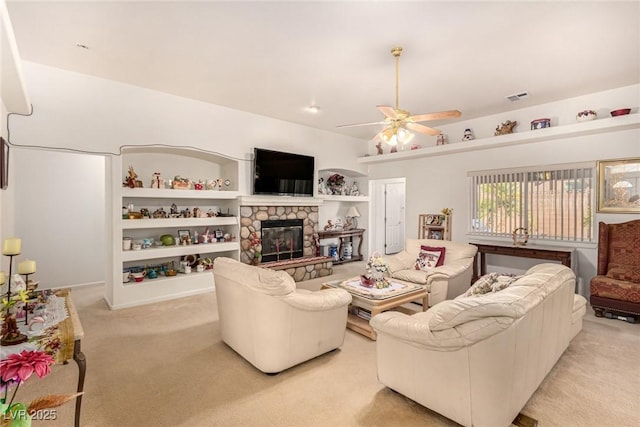 carpeted living room featuring ceiling fan, a stone fireplace, and built in shelves