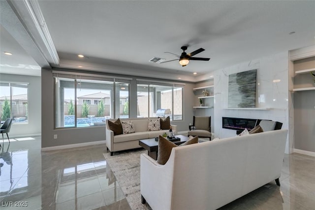 living room with a tile fireplace, ceiling fan, and crown molding