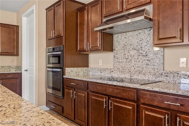 kitchen with stainless steel double oven, tasteful backsplash, light stone counters, and black electric cooktop