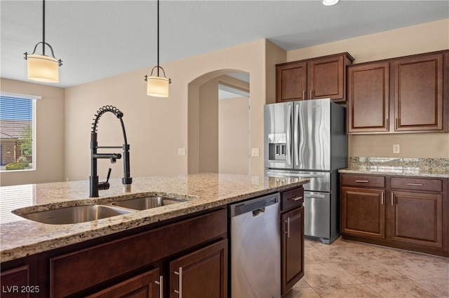 kitchen featuring light stone countertops, dark brown cabinetry, stainless steel appliances, sink, and decorative light fixtures