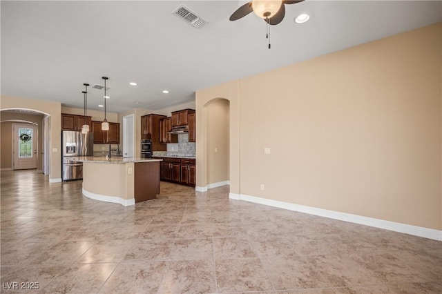 kitchen featuring light stone countertops, tasteful backsplash, stainless steel fridge with ice dispenser, hanging light fixtures, and an island with sink