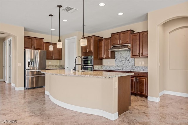 kitchen with light stone countertops, backsplash, pendant lighting, a center island with sink, and appliances with stainless steel finishes