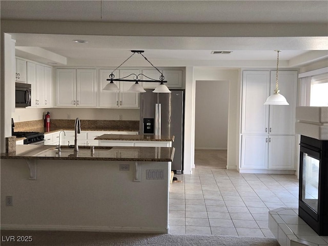 kitchen with black appliances, sink, white cabinetry, hanging light fixtures, and dark stone counters