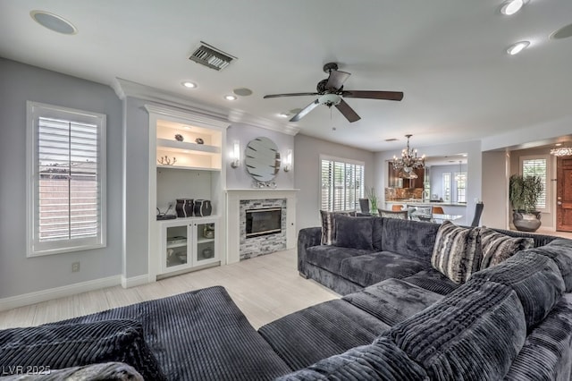 living room featuring a fireplace, ceiling fan with notable chandelier, and built in features