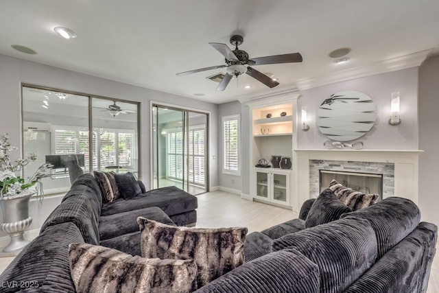 living room with plenty of natural light, a stone fireplace, light wood-type flooring, and built in shelves