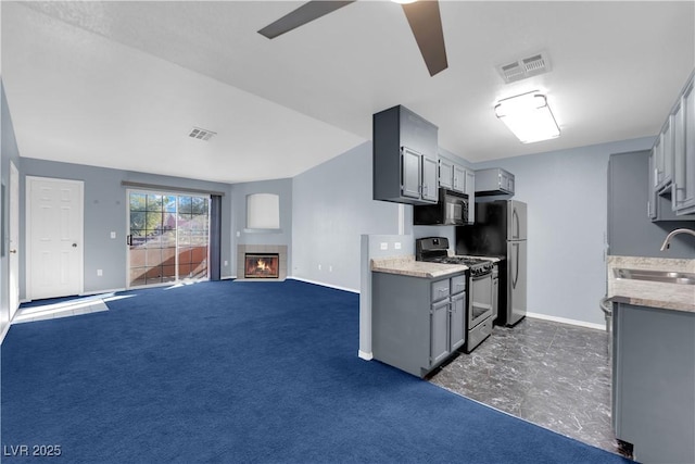 kitchen featuring sink, dark colored carpet, gray cabinets, a tiled fireplace, and appliances with stainless steel finishes