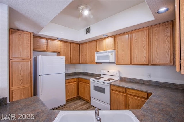 kitchen with white appliances, wood-type flooring, a raised ceiling, and sink