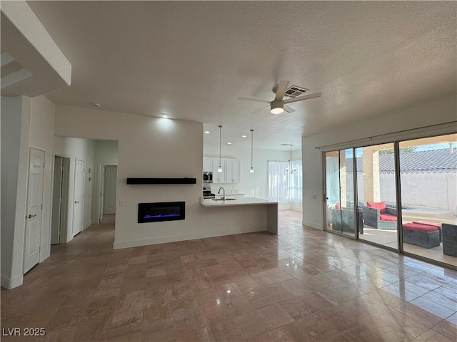 unfurnished living room with ceiling fan, sink, and a textured ceiling