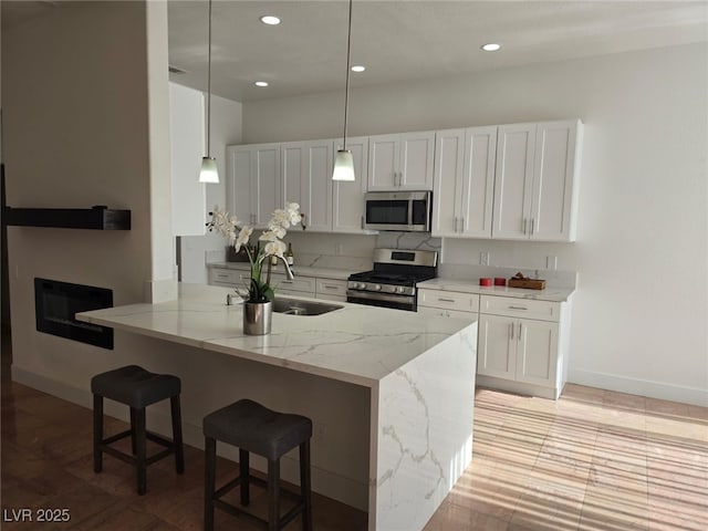 kitchen featuring hanging light fixtures, white cabinetry, light stone counters, kitchen peninsula, and stainless steel appliances