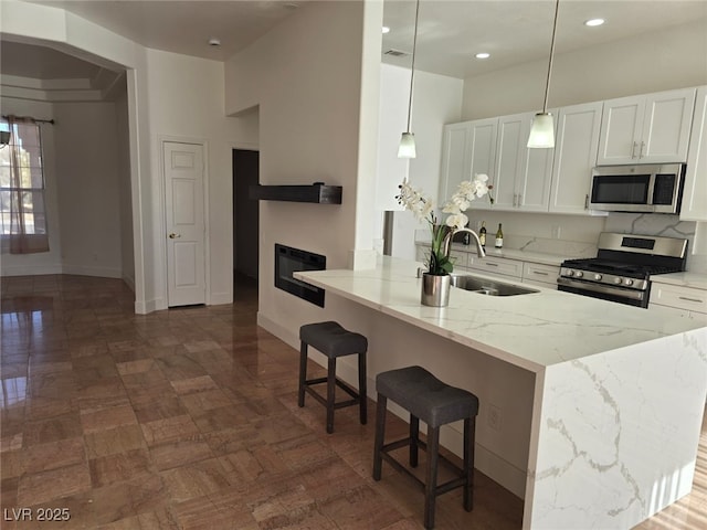 kitchen featuring white cabinetry, stainless steel appliances, light stone counters, and decorative light fixtures