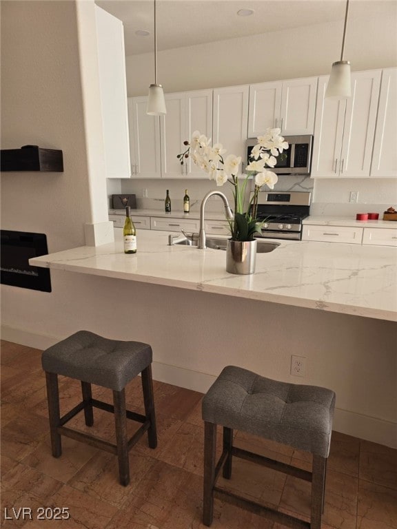 kitchen with white cabinets, decorative light fixtures, light stone counters, and appliances with stainless steel finishes