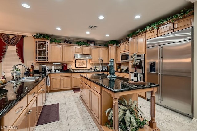 kitchen with sink, built in appliances, light tile patterned floors, and dark stone counters