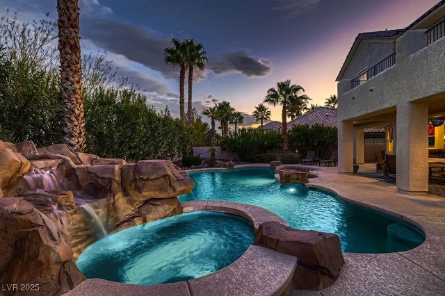 pool at dusk with an in ground hot tub, pool water feature, and a patio area