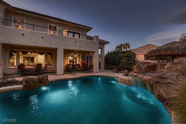 pool at dusk featuring pool water feature, ceiling fan, and a patio