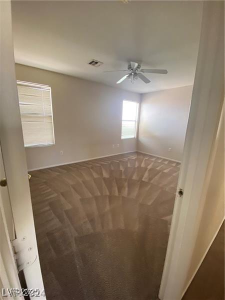 empty room featuring ceiling fan and dark colored carpet