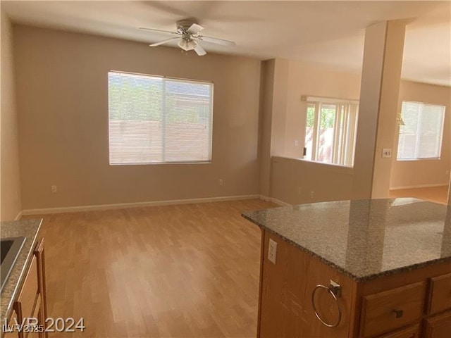 interior space with ceiling fan, dark stone countertops, and light hardwood / wood-style flooring