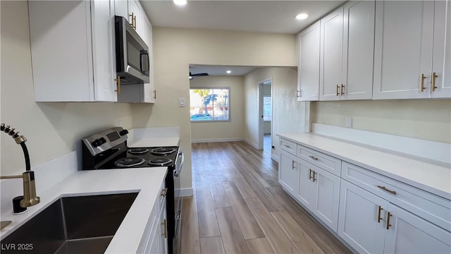 kitchen featuring light wood-type flooring, ceiling fan, sink, electric stove, and white cabinets