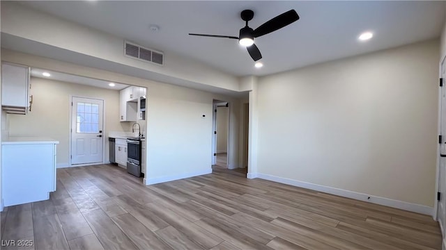 interior space with white cabinets, sink, light hardwood / wood-style flooring, and stainless steel range oven