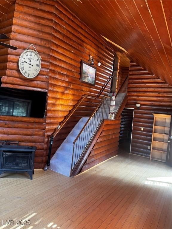 stairs with a wood stove, log walls, wooden ceiling, and wood-type flooring