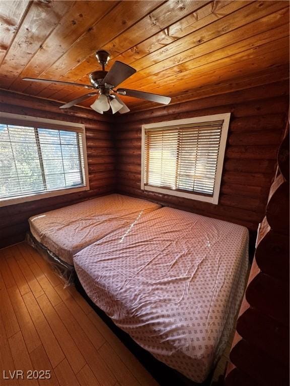 bedroom featuring log walls, hardwood / wood-style floors, ceiling fan, and wood ceiling