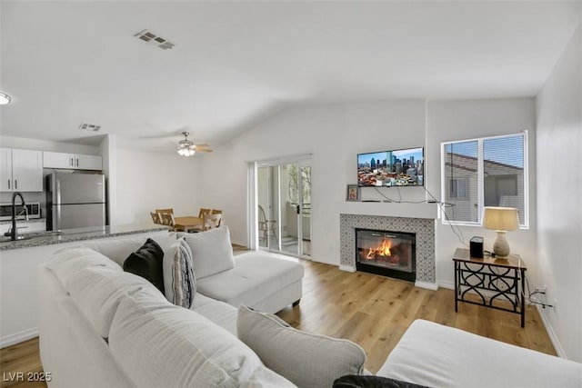 living room with ceiling fan, plenty of natural light, a tile fireplace, and vaulted ceiling