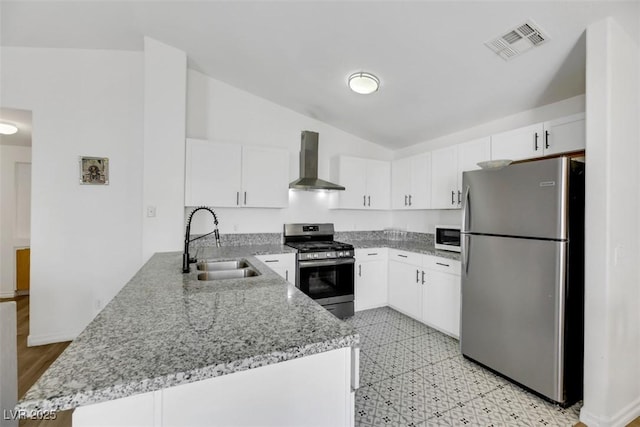 kitchen featuring wall chimney range hood, sink, appliances with stainless steel finishes, white cabinetry, and kitchen peninsula