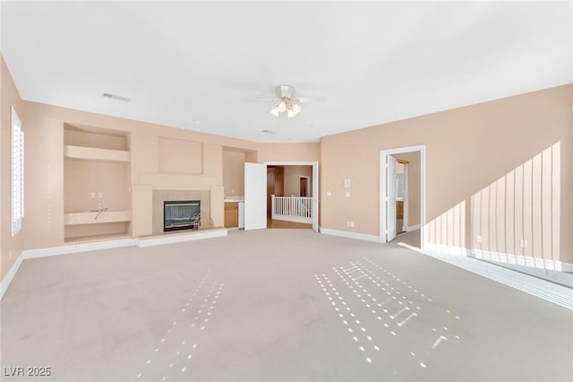 unfurnished living room featuring ceiling fan, light colored carpet, and built in shelves