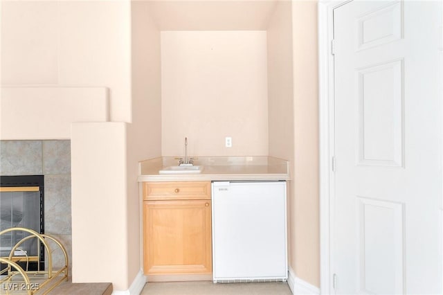 bar featuring sink, white dishwasher, a tiled fireplace, and light brown cabinetry