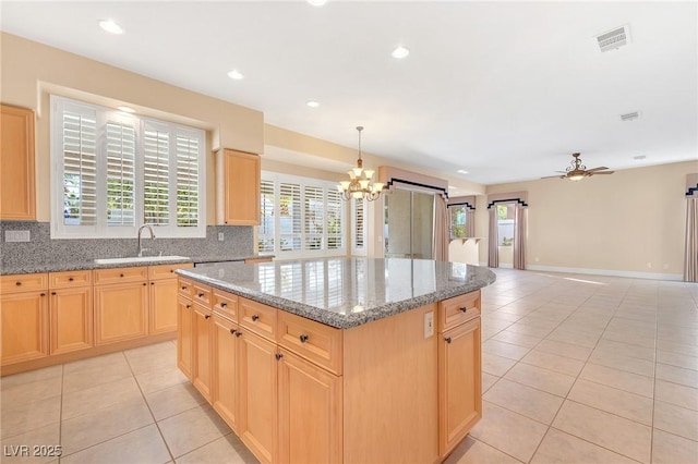 kitchen featuring light stone counters, a center island, ceiling fan with notable chandelier, light tile patterned flooring, and sink