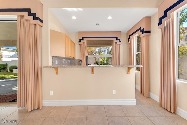 kitchen featuring kitchen peninsula, light brown cabinetry, a breakfast bar, and tasteful backsplash