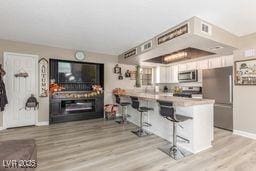 kitchen with a breakfast bar, kitchen peninsula, appliances with stainless steel finishes, light hardwood / wood-style floors, and white cabinetry