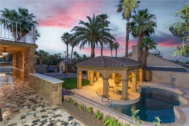 pool at dusk featuring a gazebo and a patio