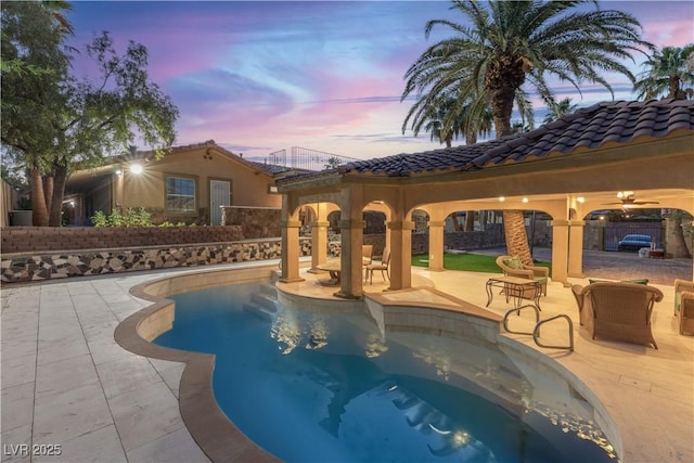 pool at dusk with ceiling fan and a patio