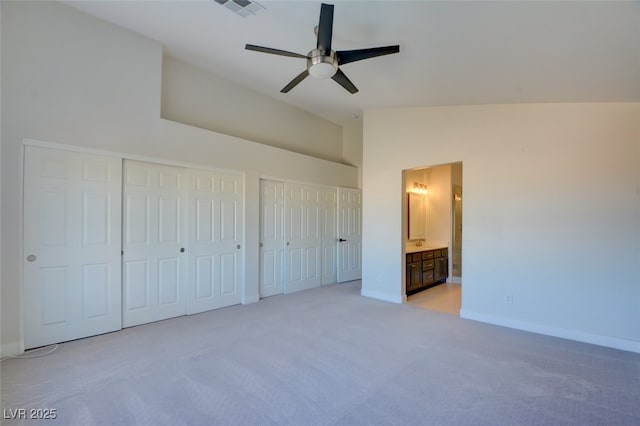 unfurnished bedroom with ensuite bath, two closets, vaulted ceiling, light colored carpet, and ceiling fan