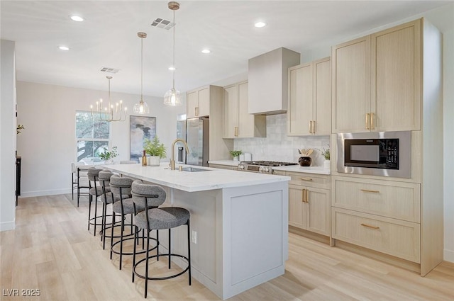 kitchen with pendant lighting, premium range hood, a kitchen island with sink, built in microwave, and tasteful backsplash