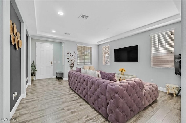 living room with light hardwood / wood-style floors and a tray ceiling