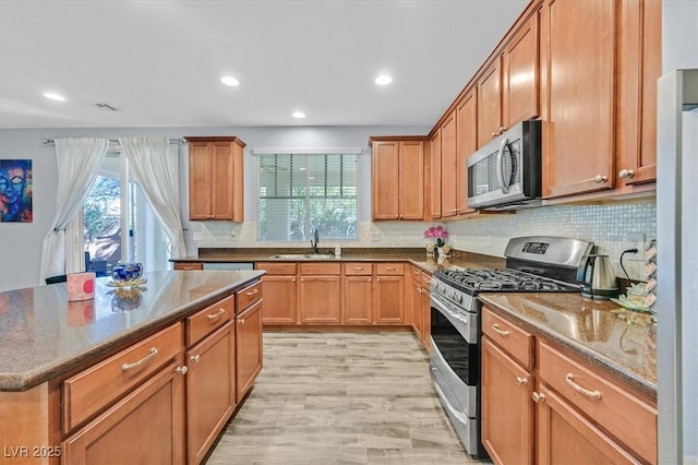 kitchen featuring sink, light wood-type flooring, appliances with stainless steel finishes, tasteful backsplash, and a kitchen island