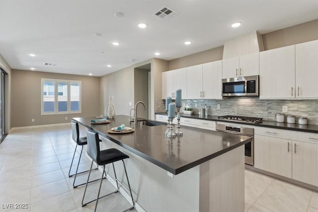 kitchen featuring an island with sink, appliances with stainless steel finishes, sink, and a breakfast bar