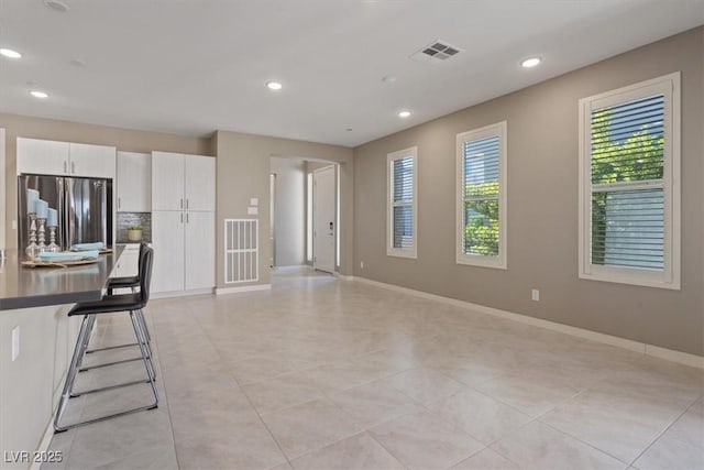 kitchen featuring white cabinetry, stainless steel fridge, a breakfast bar, and decorative backsplash