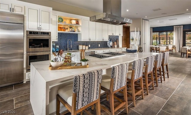 kitchen with a breakfast bar area, white cabinetry, island range hood, appliances with stainless steel finishes, and backsplash