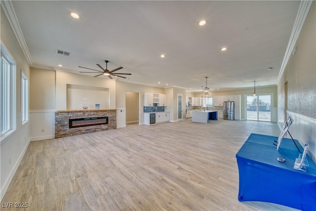 unfurnished living room featuring ornamental molding, a stone fireplace, ceiling fan, and light wood-type flooring