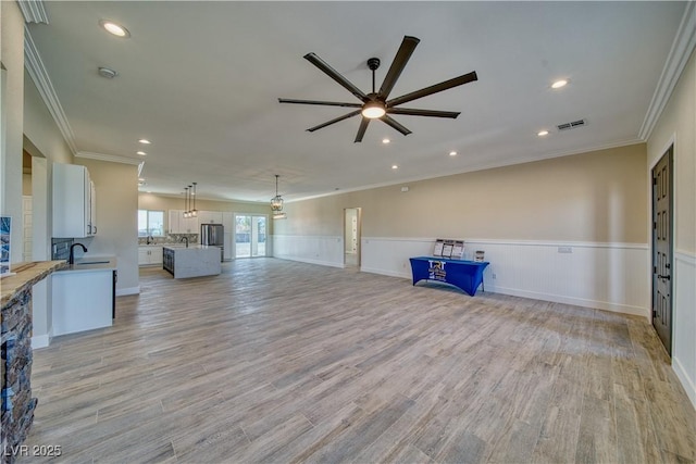 unfurnished living room featuring ceiling fan, ornamental molding, light hardwood / wood-style floors, and sink