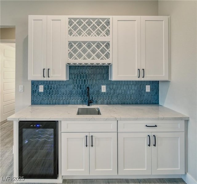 kitchen with wine cooler, white cabinetry, sink, and light stone counters