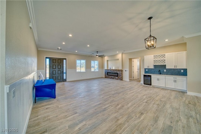 unfurnished living room featuring sink, crown molding, light hardwood / wood-style flooring, wine cooler, and a fireplace